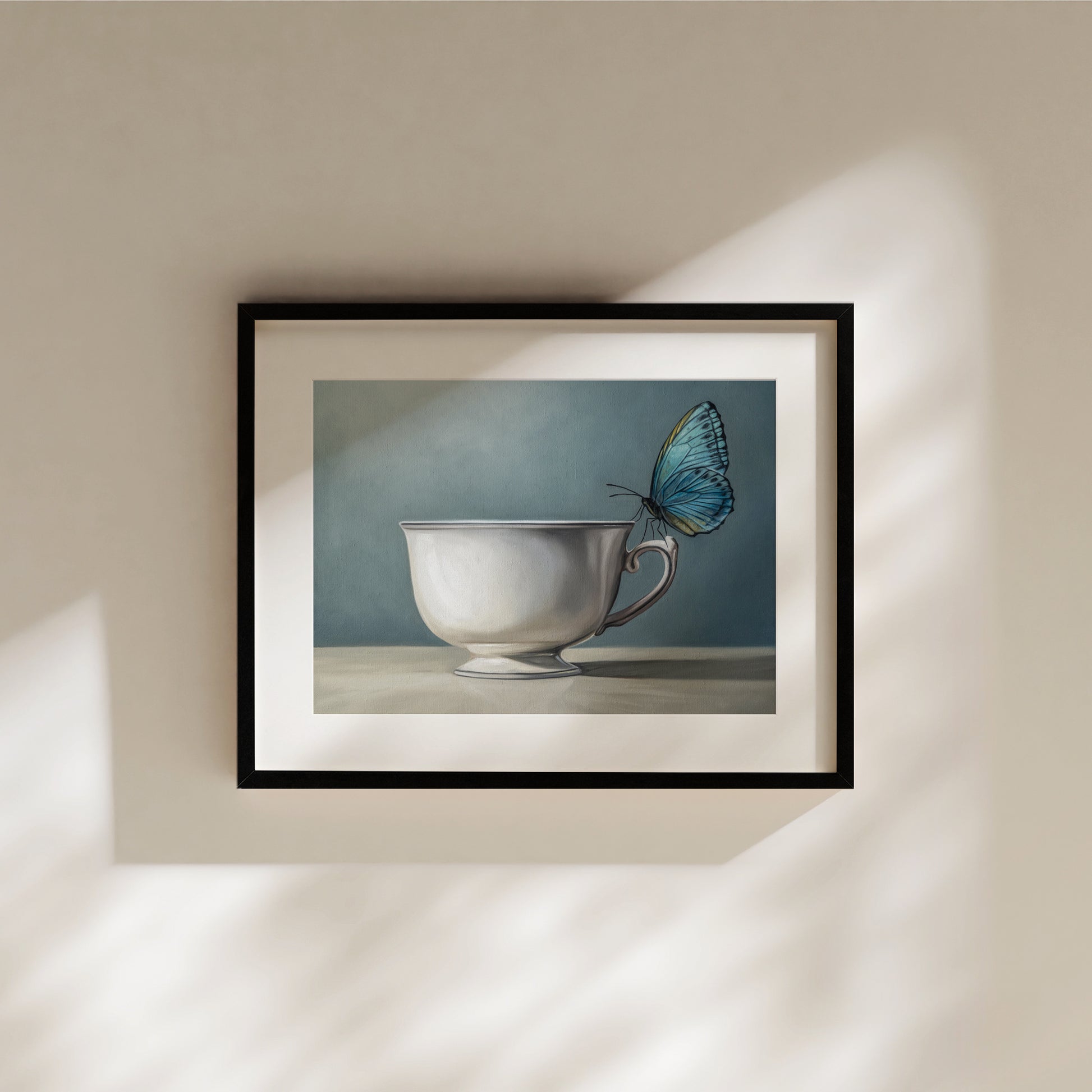 Framed fine art print of a blue butterfly perched on a white teacup against a muted blue background.