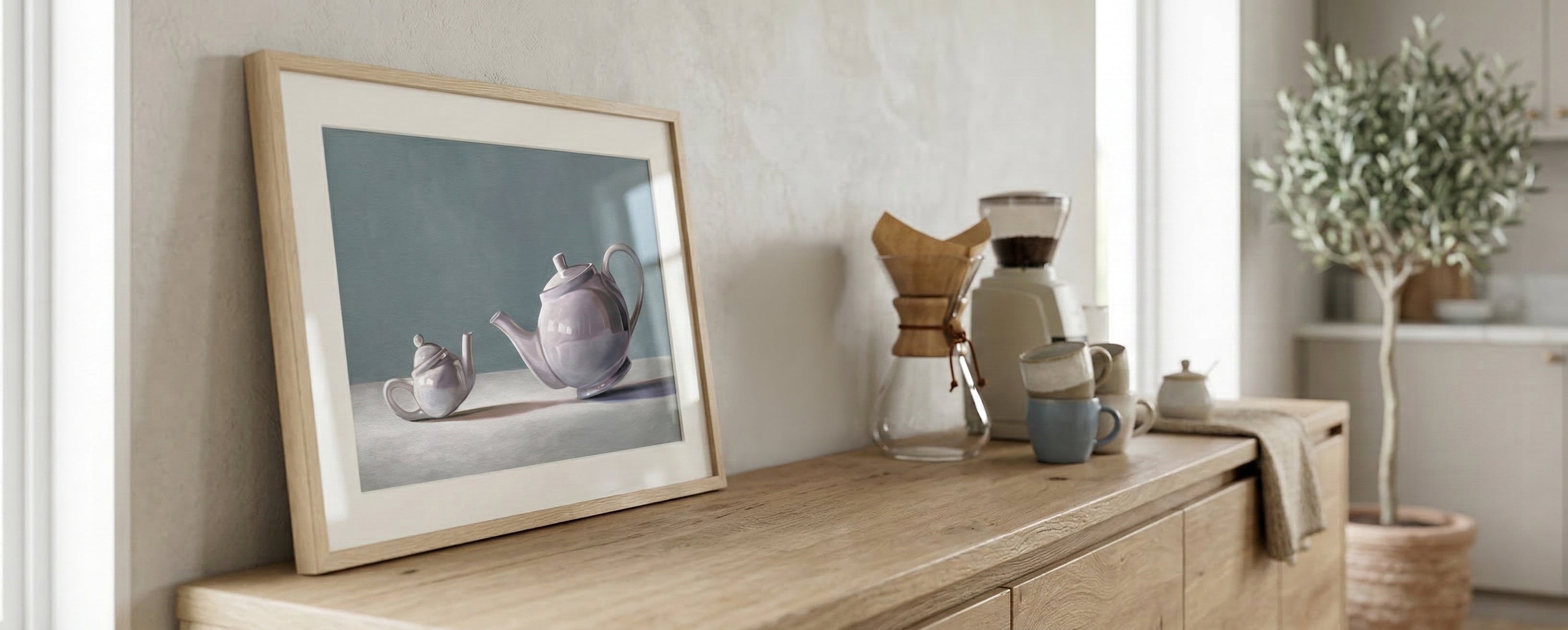 Framed artwork with a teapot and tiny teapot on a wooden surface with decorative items