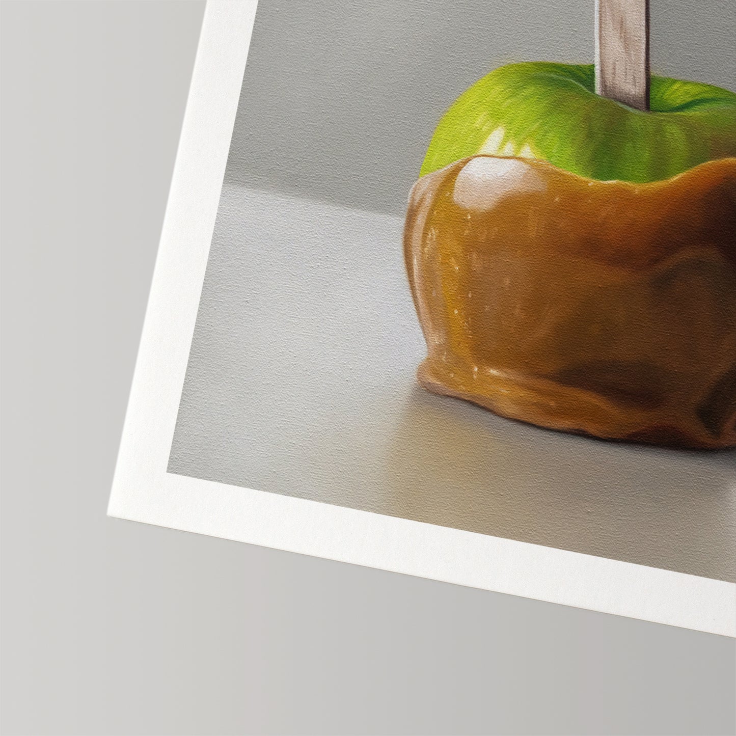 Fine art print of a vibrant green caramel apple on a stick, featuring a textured paper border.