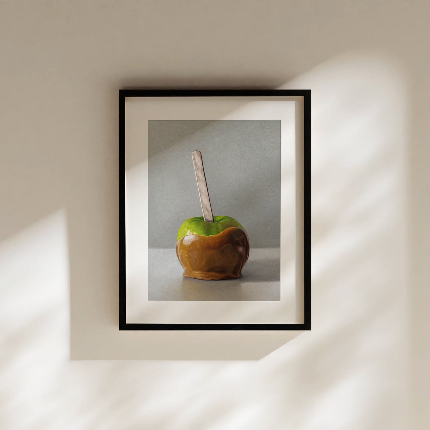 Framed fine art print of a vibrant green caramel apple with a wooden stick, on a light background.