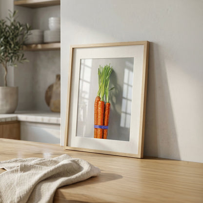 Framed fine art print of a vibrant carrot bunch tied with a blue band, displayed on a light wood counter.