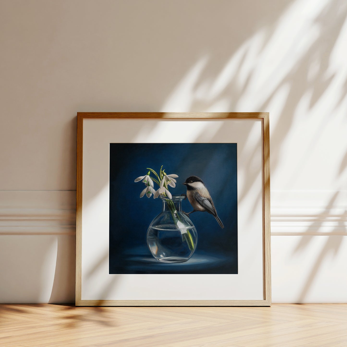 Framed fine art print of a chickadee perched on a clear vase with white snowdrop flowers against a dark blue background.