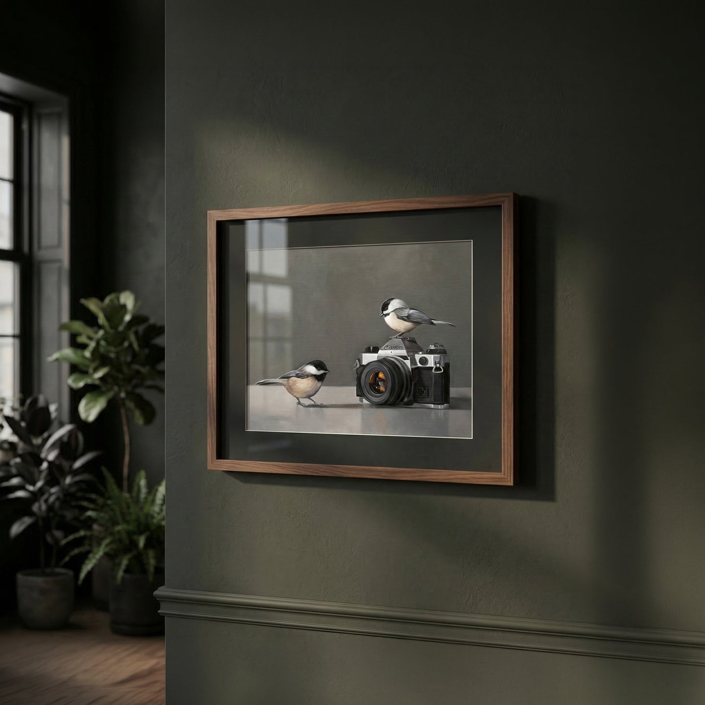 Fine art print of two chickadees with a vintage camera, framed in dark wood, on a dark green wall.