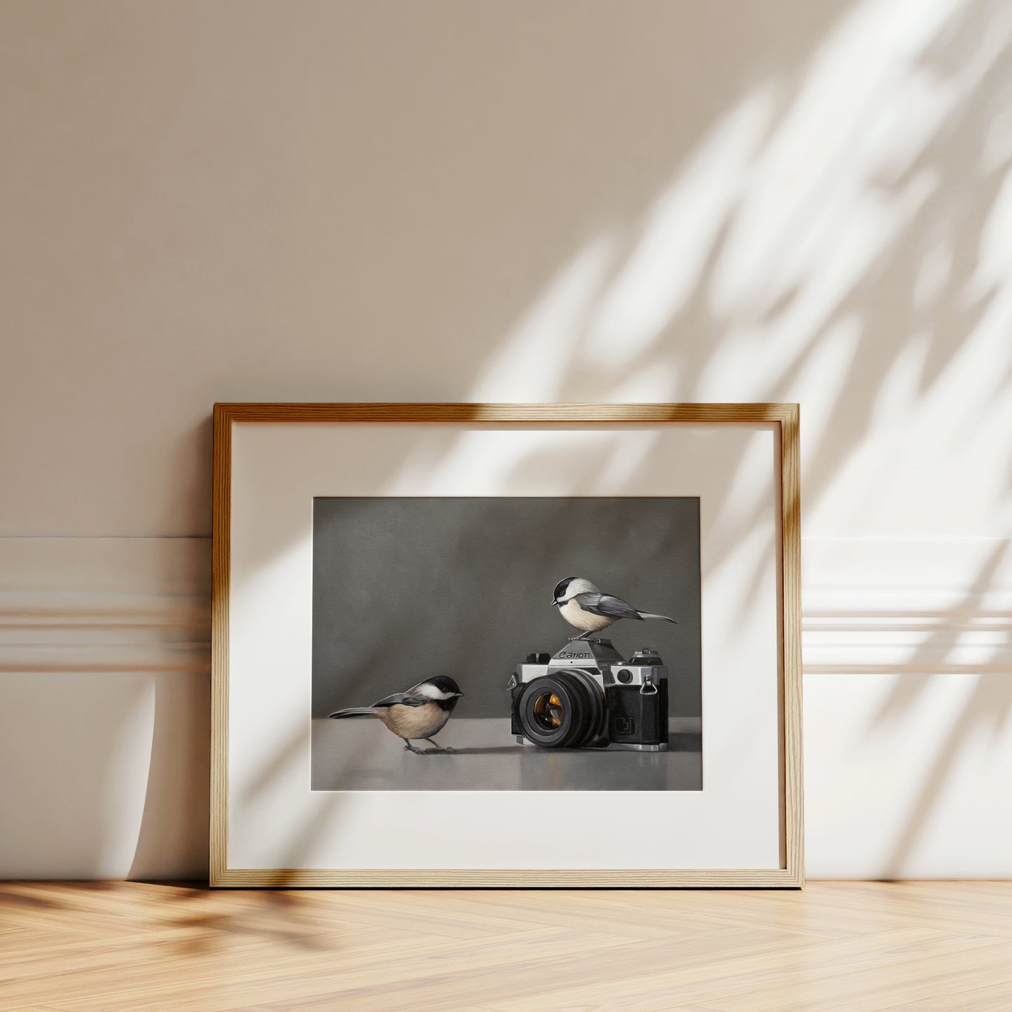 Fine art print featuring two chickadees with a vintage camera, framed in light wood.