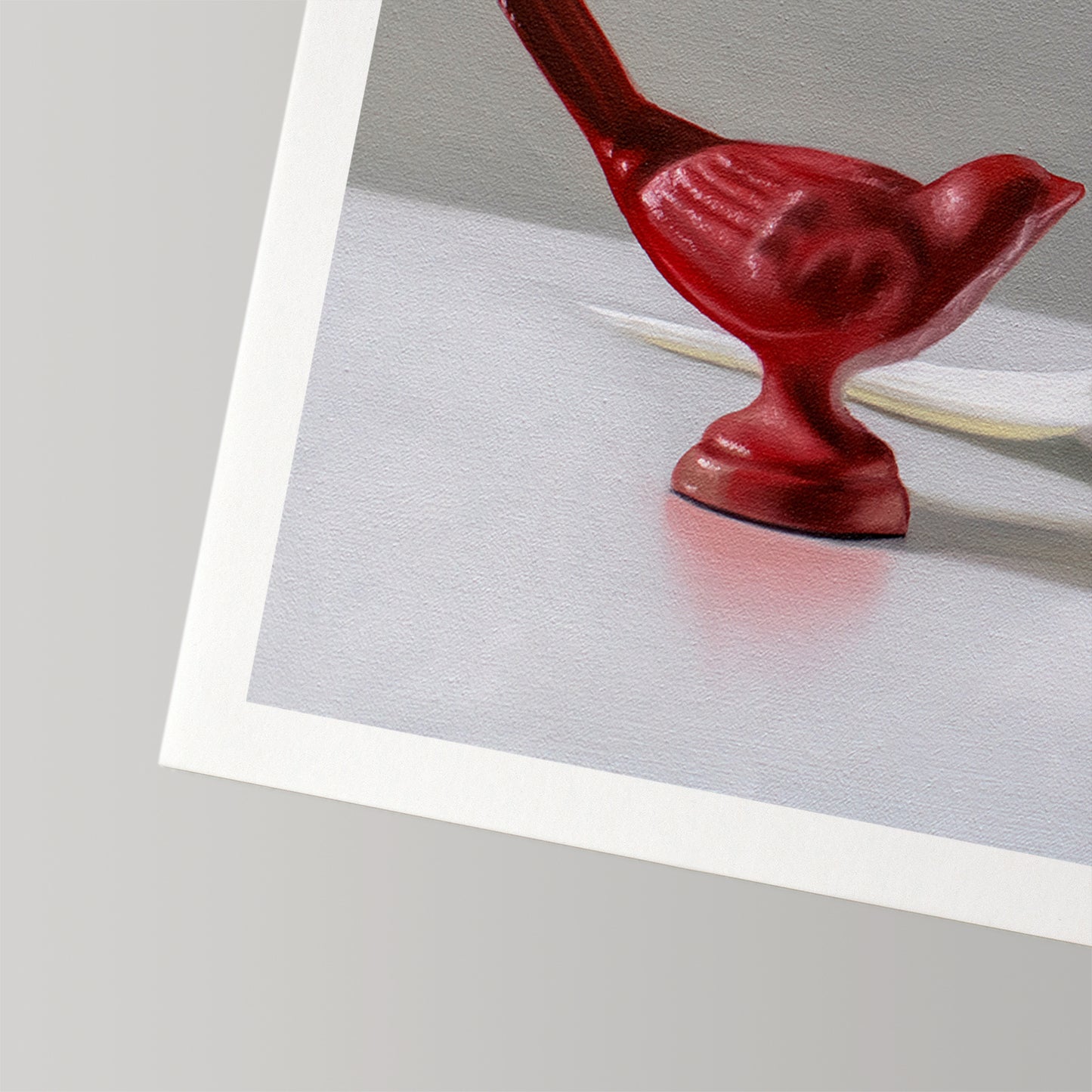 Fine art print of a glossy red bird figurine on a white surface, with a white border.