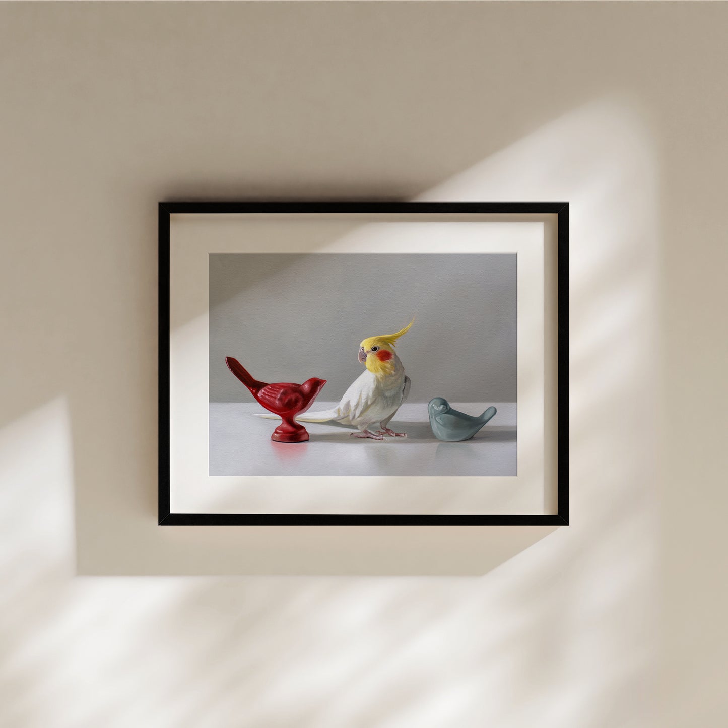 Fine art print of a cockatiel with red and blue bird figurines, framed in black.