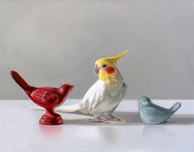 Realistic oil painting of a white and yellow cockatiel standing between red and blue ceramic bird figurines.