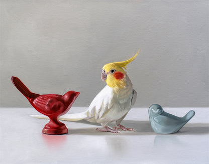 Realistic oil painting of a white and yellow cockatiel standing between red and blue ceramic bird figurines.