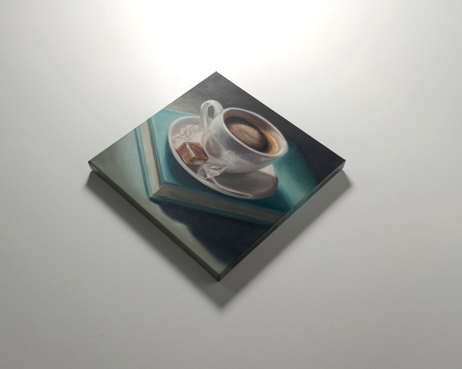 Coffee, Caramel & Book 12" x 12" Original Oil Painting by Lauren Pretorius: a white cup of coffee with a saucer on top of a book, with a piece of caramel on the saucer.