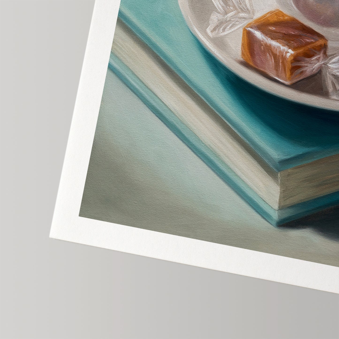 Fine art print of a caramel candy on a white plate, resting on two teal books, with a white border.