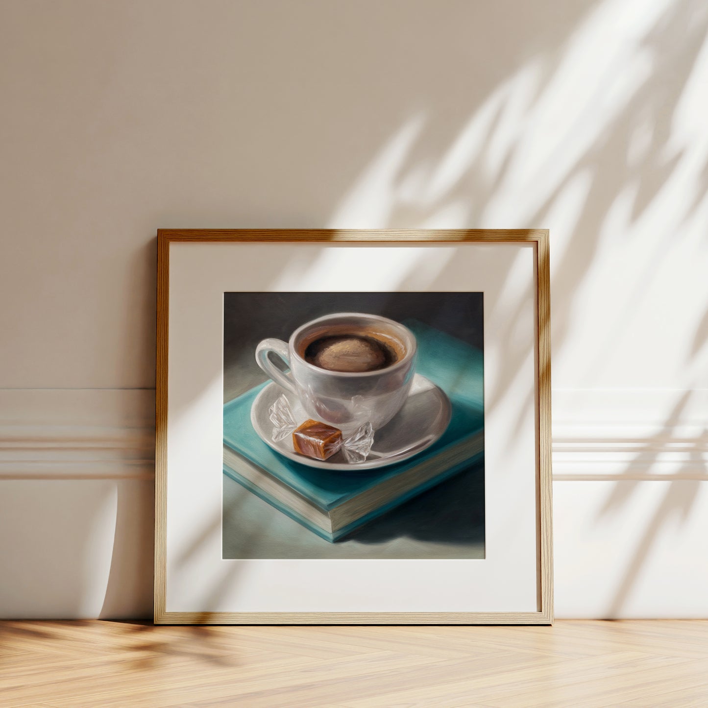 Framed art print of a white coffee cup, caramel candy, and a teal book, with sun shadows.