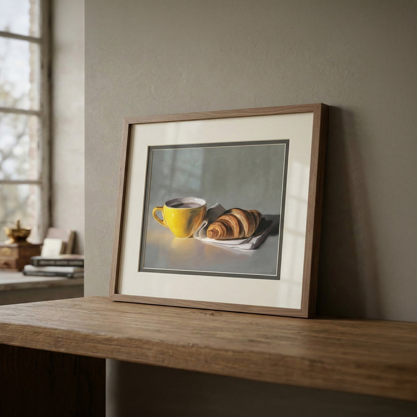 Framed fine art print of a yellow coffee cup and croissant on a white napkin, displayed on a wooden surface.