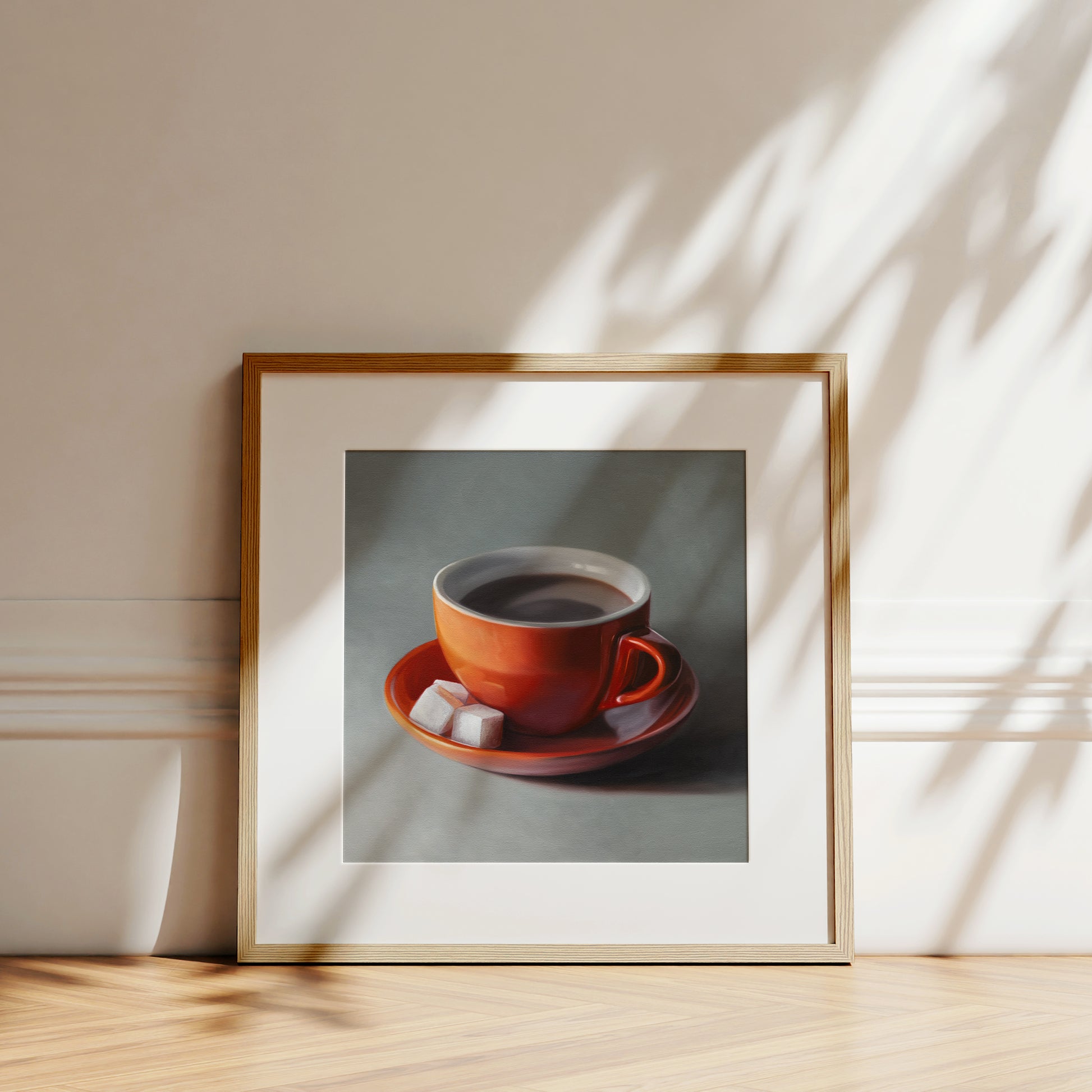 Fine art print of a vibrant orange coffee cup and saucer with two white sugar cubes, framed in light wood.