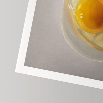 Fine art print of a cracked egg with a vibrant yellow yolk and clear white on a gray background, featuring a white border.