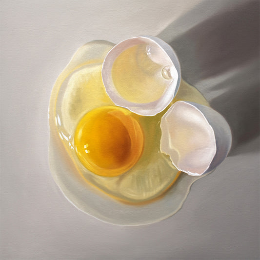 Overhead view of a cracked egg with a bright yellow yolk and white shell pieces on a light gray surface.