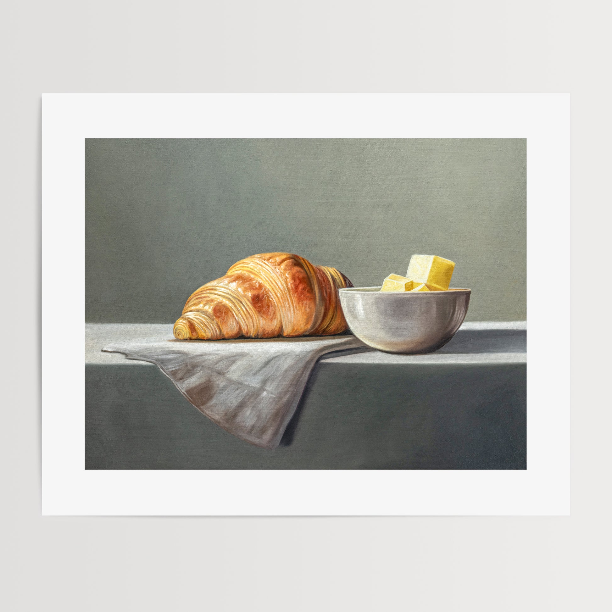 Croissant & Butter Fine Art Print by Lauren Pretorius: a croissant and a block of butter on a white surface with a grey background.