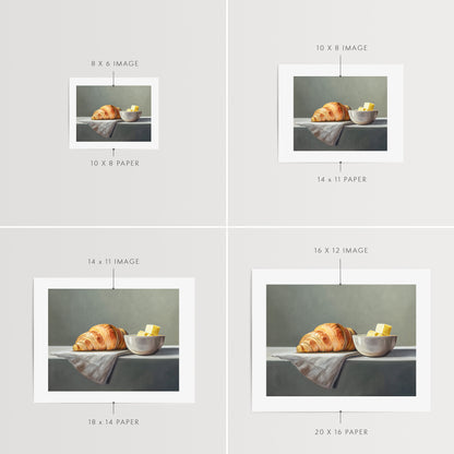 Croissant & Butter Fine Art Print by Lauren Pretorius: a croissant and a block of butter on a white surface with a grey background.