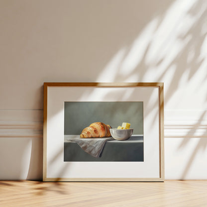 Croissant & Butter Fine Art Print by Lauren Pretorius: a croissant and a block of butter on a white surface with a grey background.