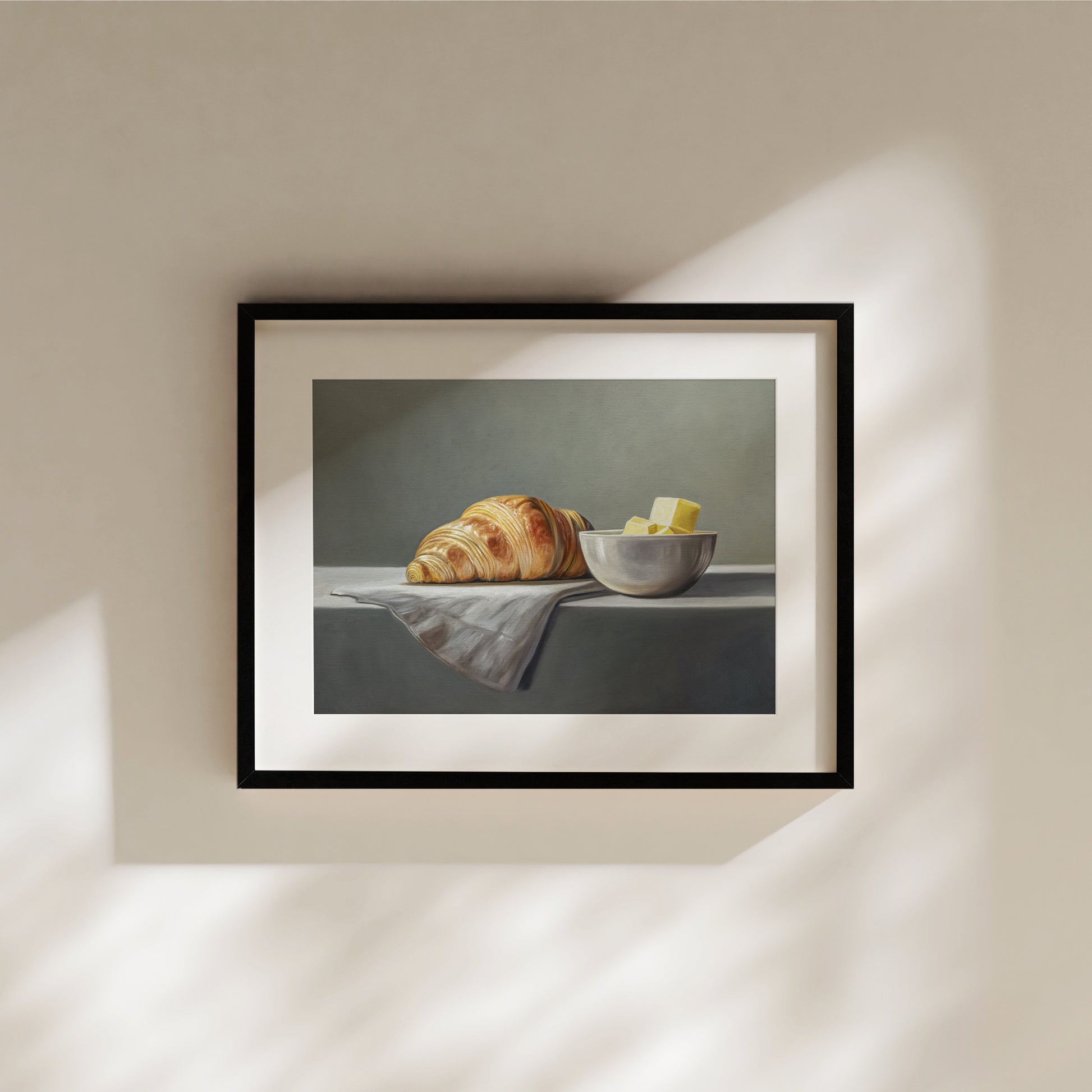 Croissant & Butter Fine Art Print by Lauren Pretorius: a croissant and a block of butter on a white surface with a grey background.