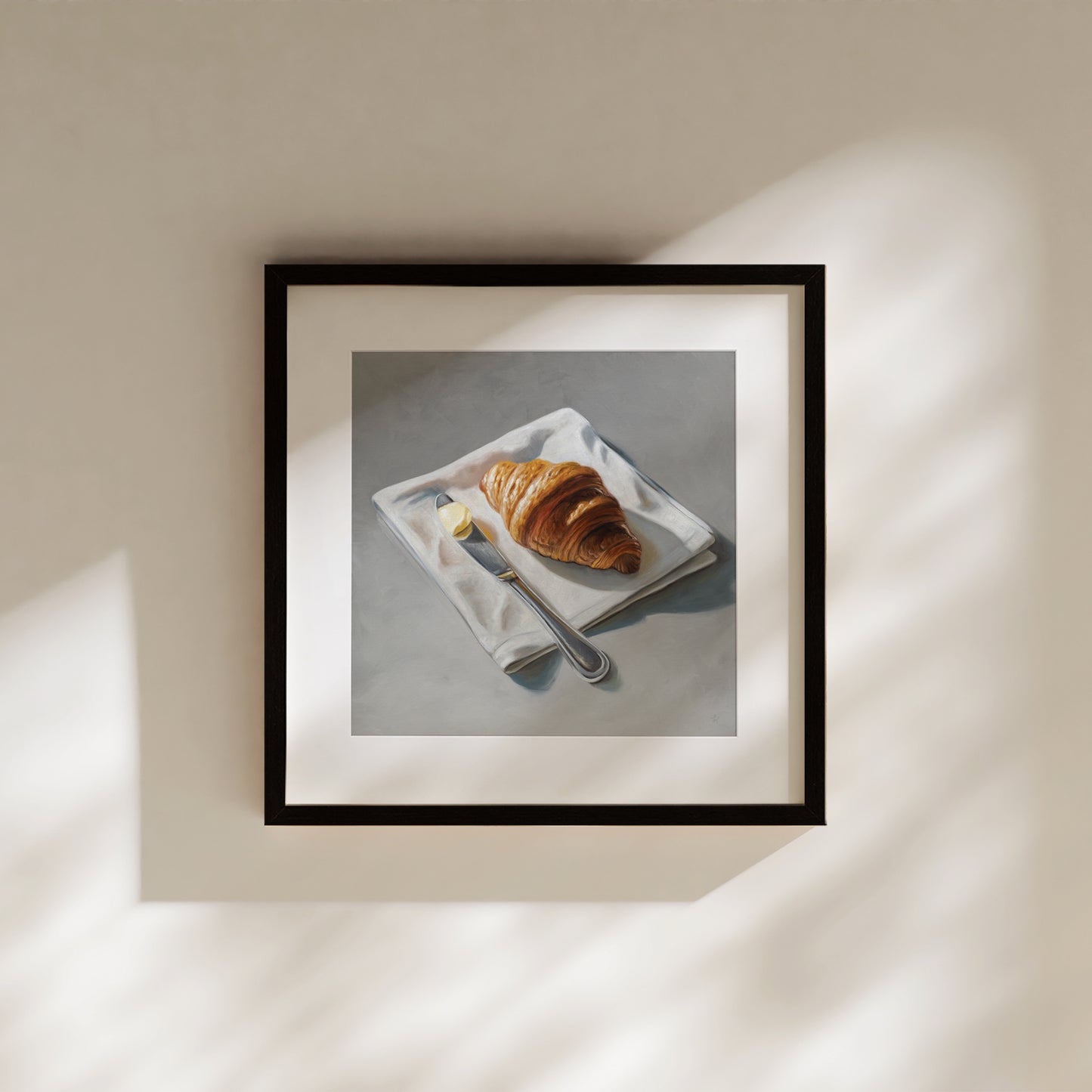Framed fine art print of a golden croissant, butter, and knife on a white napkin, against a gray background.