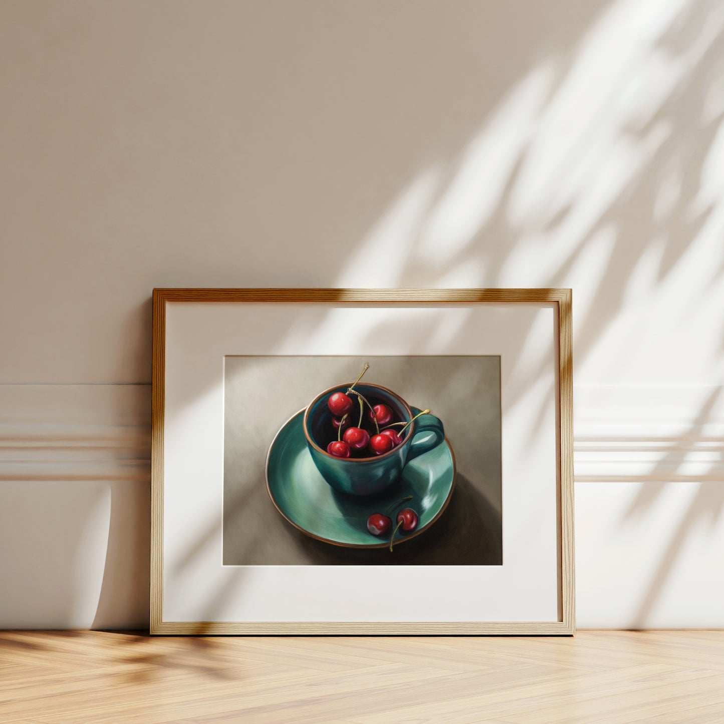 Cup of Cherries Fine Art Print by Lauren Pretorius: red cherries inside a blue green ceramic cup with a matching saucer, with a few cherries scattered outside the cup on a grey surface.