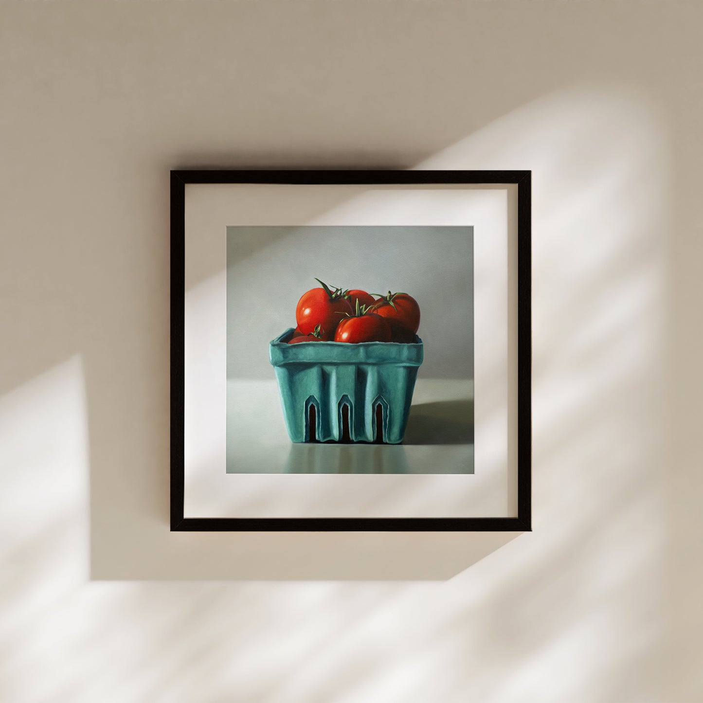 Framed fine art print of vibrant red tomatoes in a teal berry basket, hanging on a light wall.