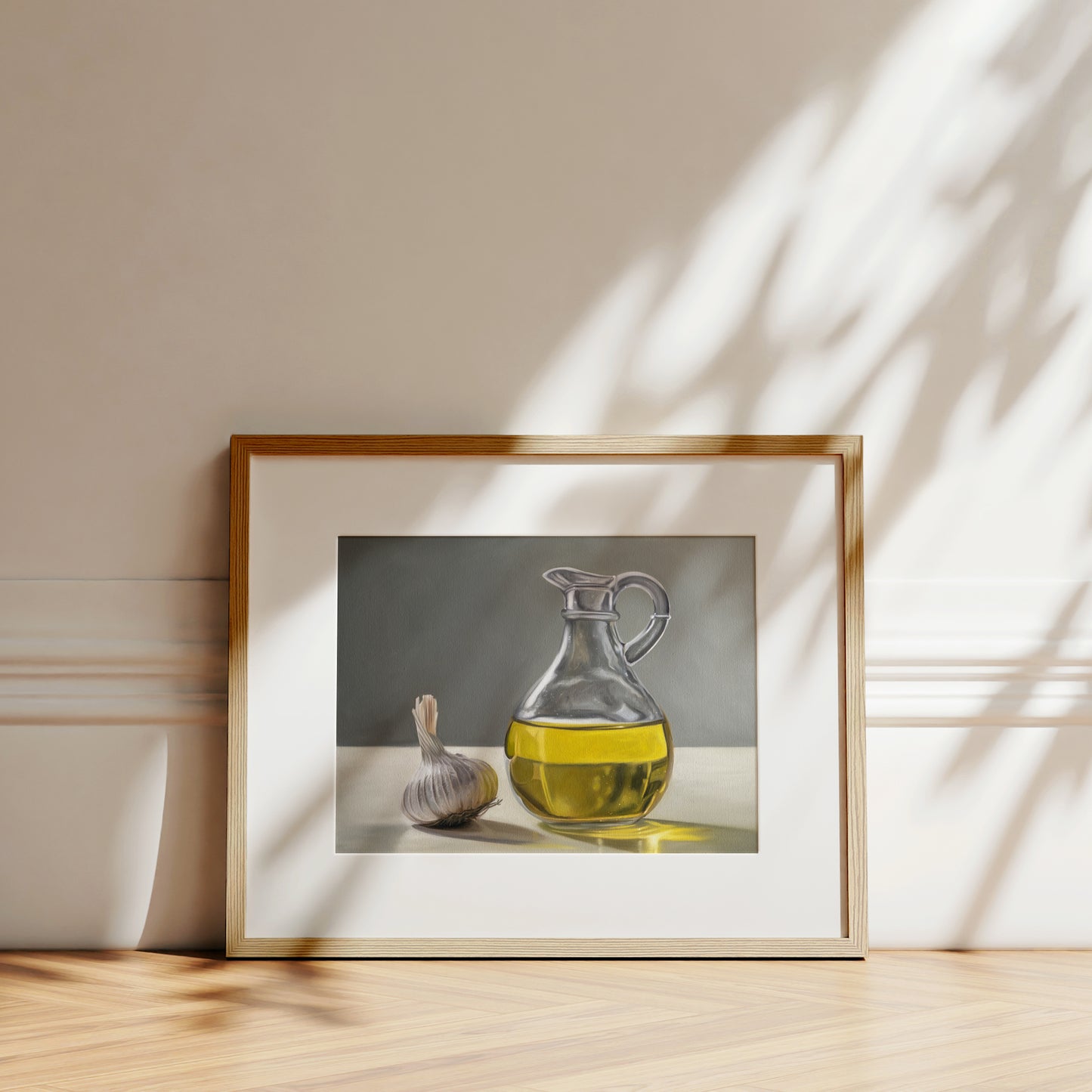 Framed fine art print of a garlic bulb and a clear glass carafe of golden olive oil on a white table.
