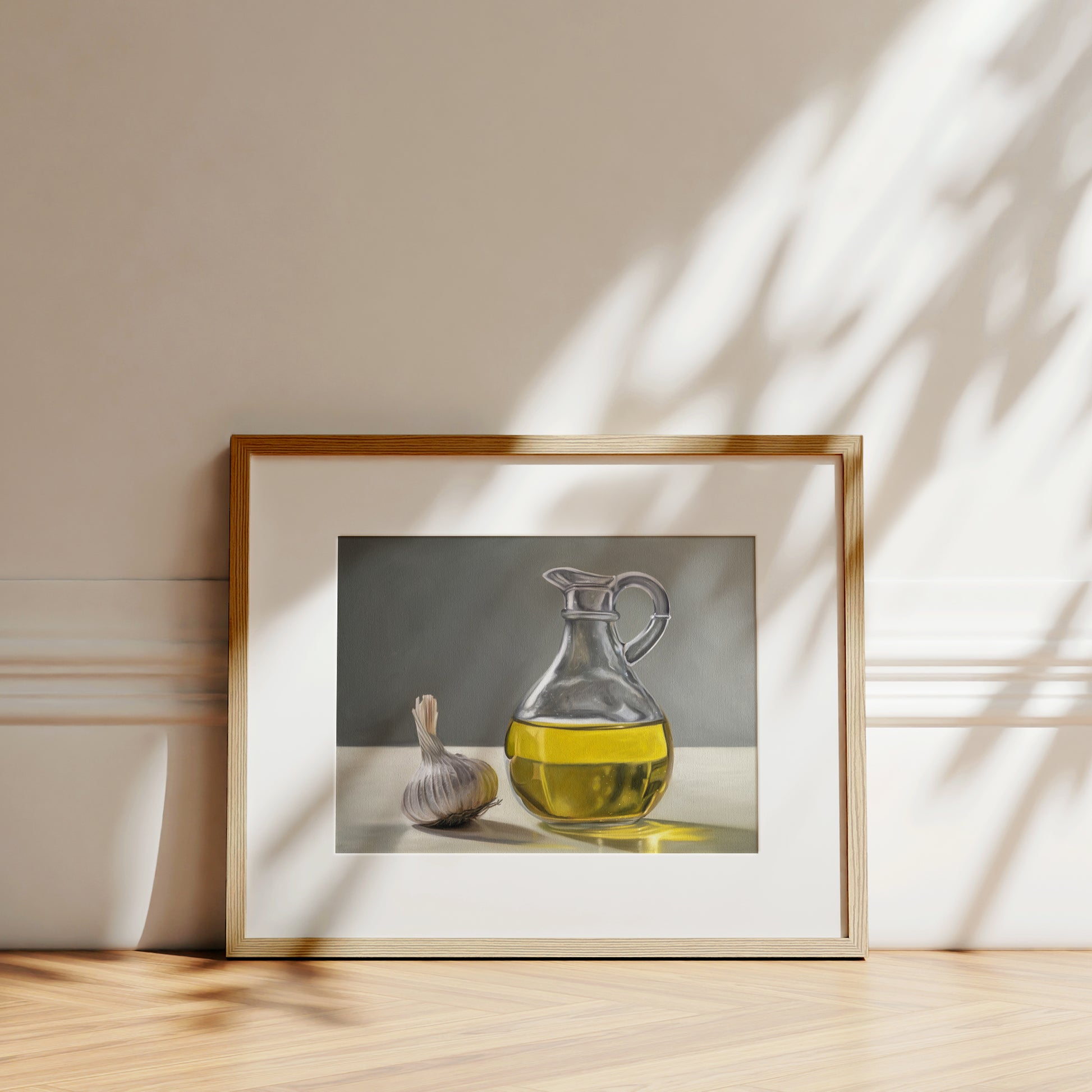 Framed fine art print of a garlic bulb and a clear glass carafe of golden olive oil on a white table.