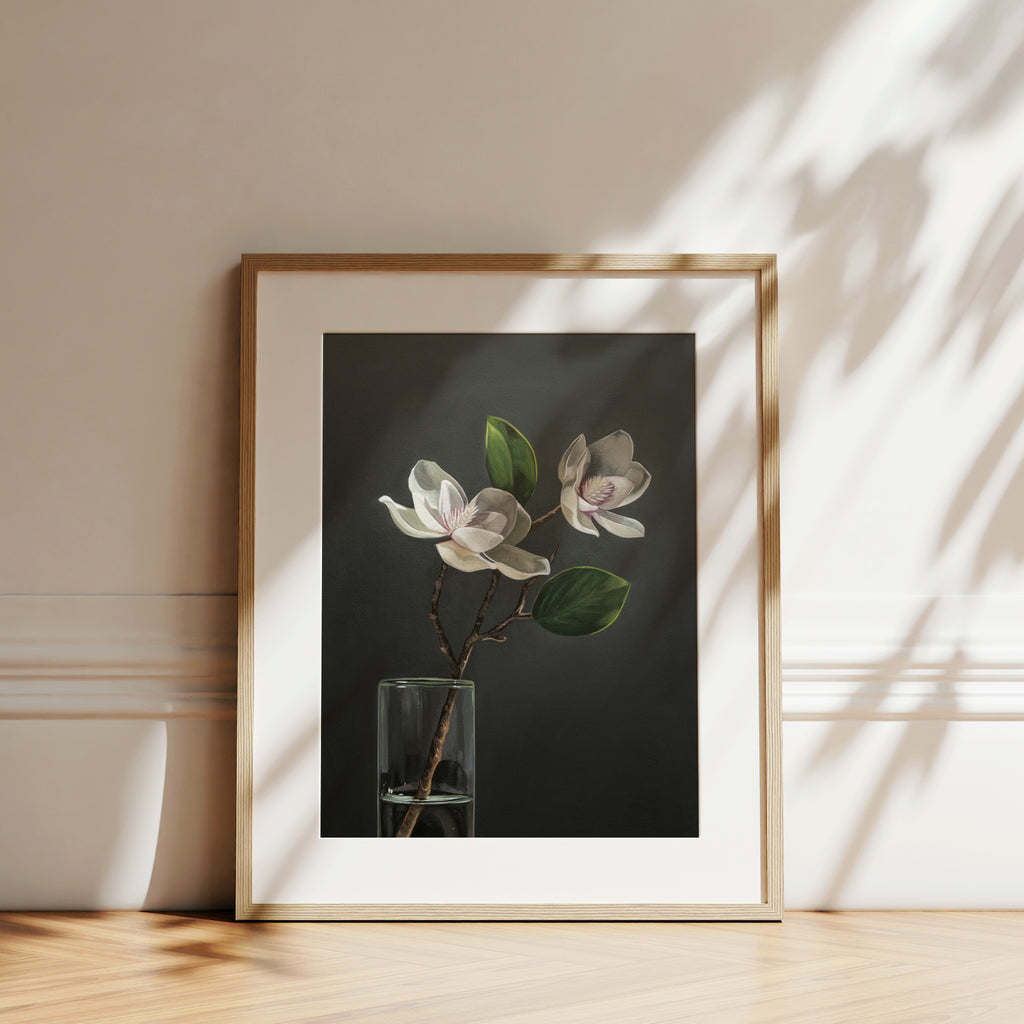 This artwork features a duo of magnolia blooms in a slim glass vase set against a dark backdrop.