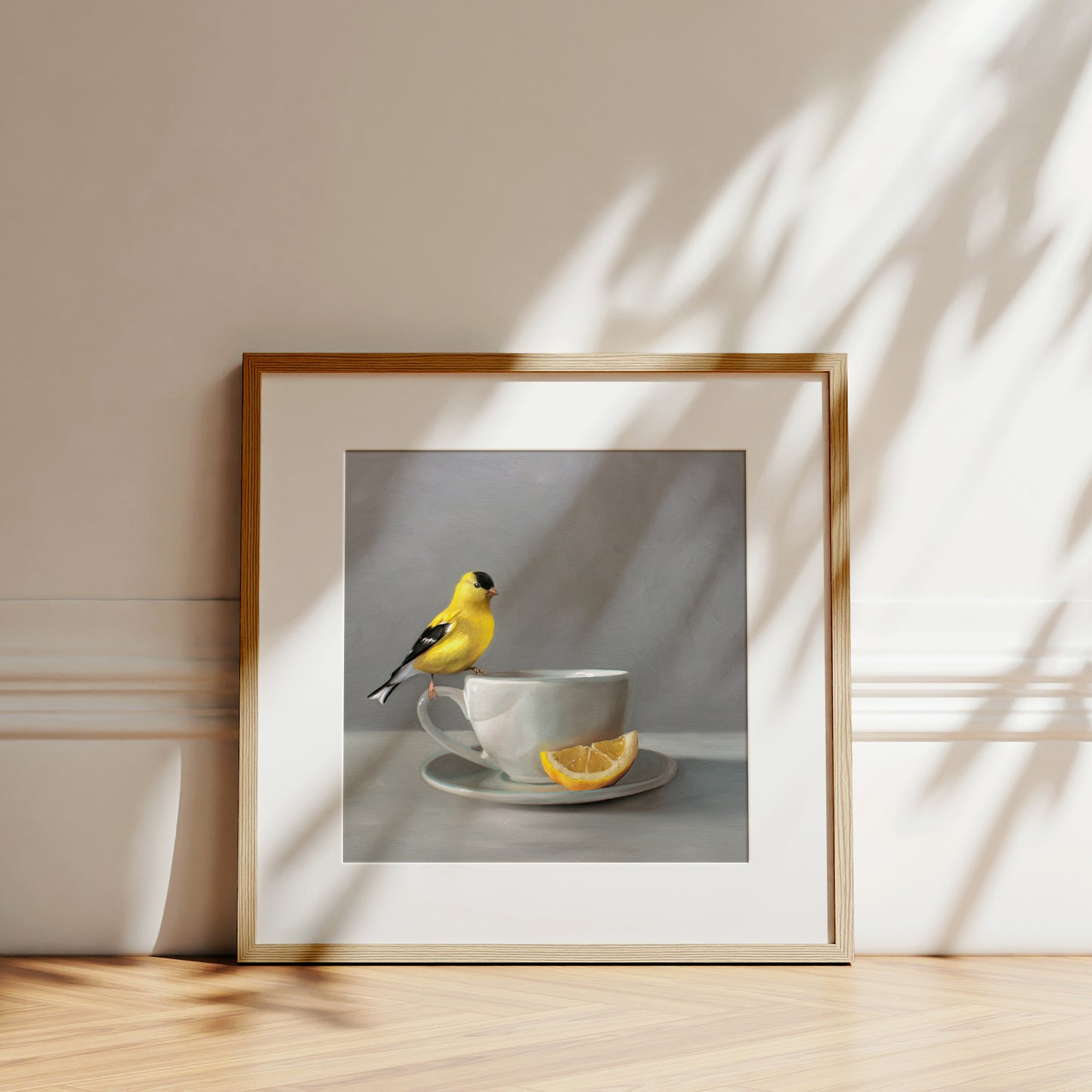 Framed fine art print of a vibrant yellow goldfinch perched on a white teacup with a lemon slice.