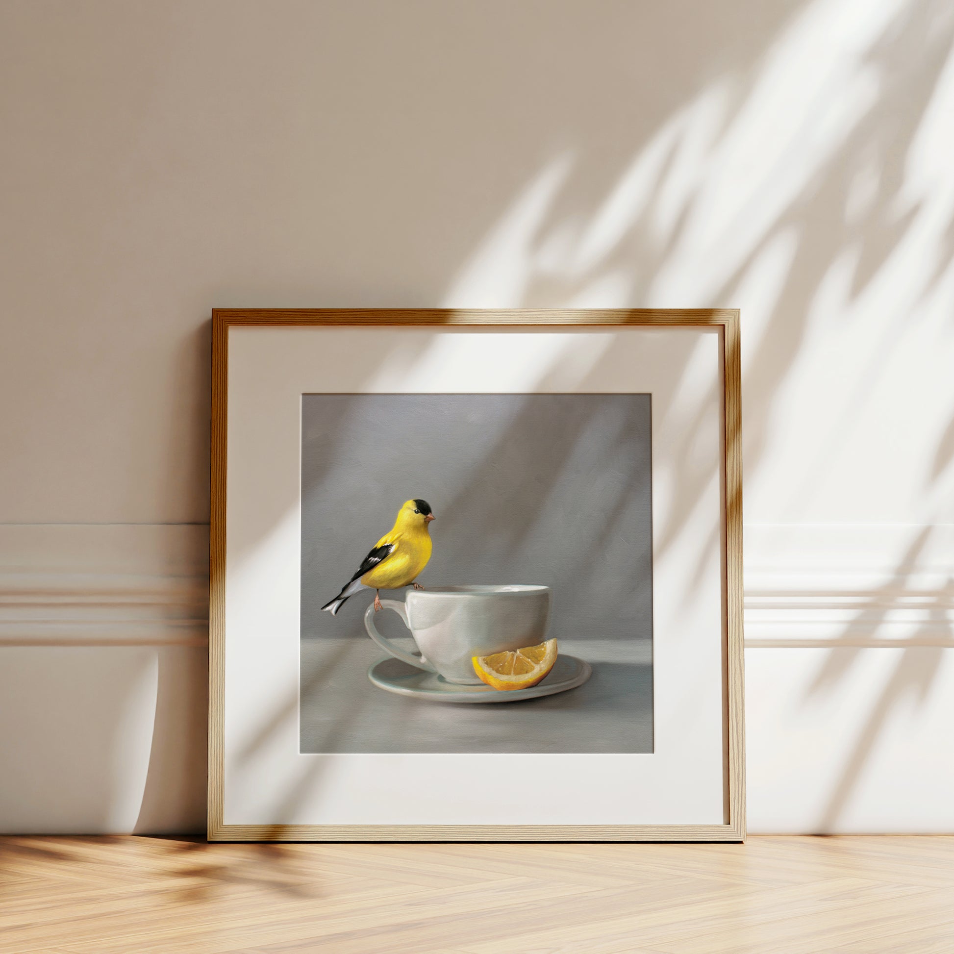 Framed fine art print of a vibrant yellow goldfinch perched on a white teacup with a lemon slice.