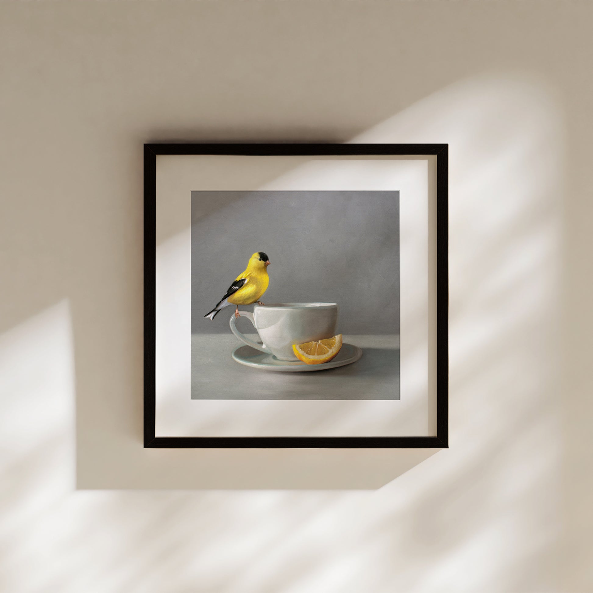 Framed fine art print of a yellow goldfinch perched on a grey teacup with a lemon slice.