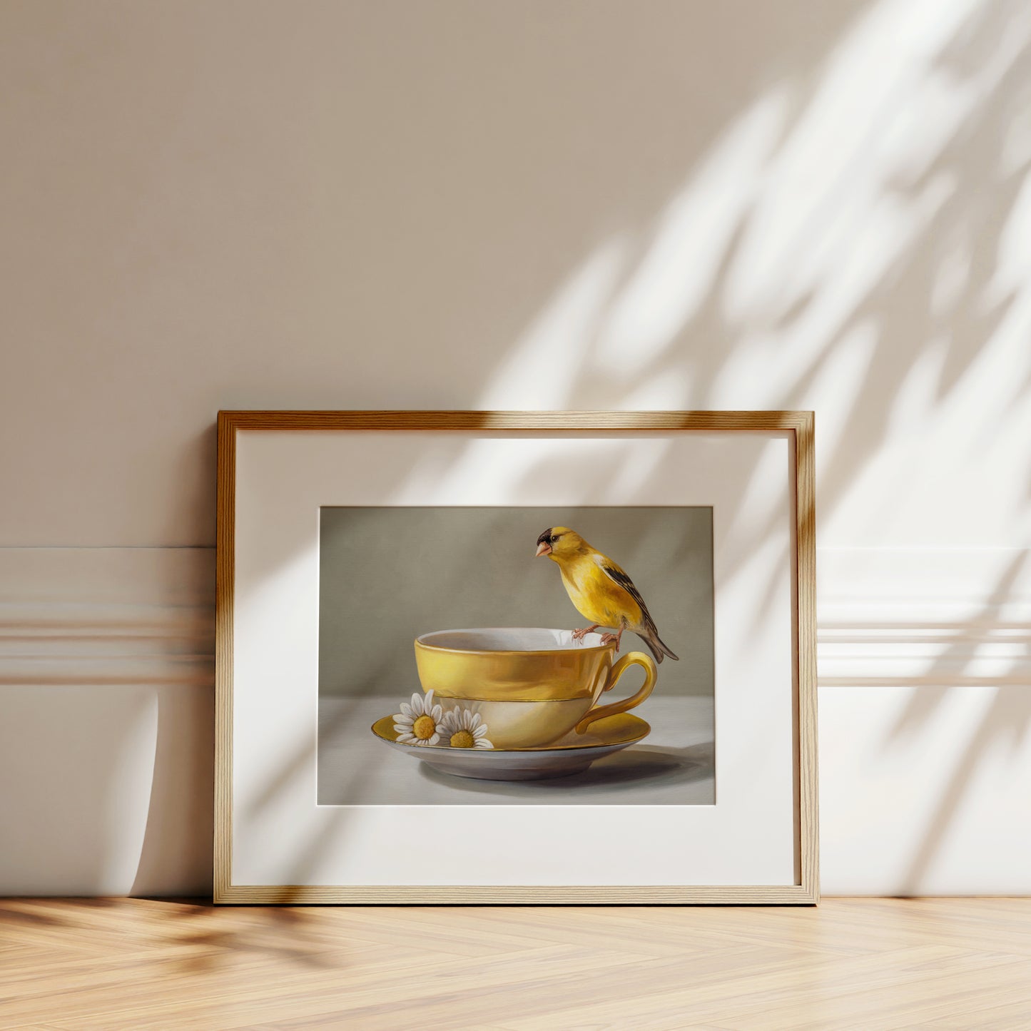 Goldfinch & Yellow Cup Fine Art Print by Lauren Pretorius: a goldfinch perched on a gold teacup with white flowers on a saucer against a neutral background