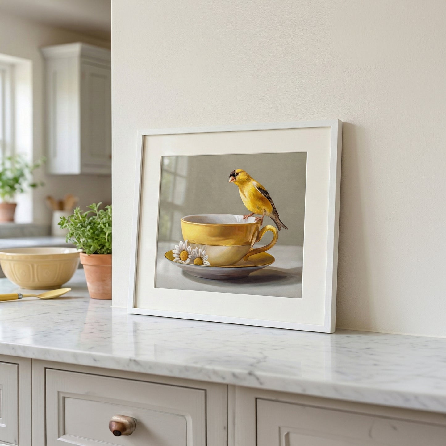Framed fine art print of a yellow goldfinch perched on stacked yellow teacups with daisies, on a marble counter.