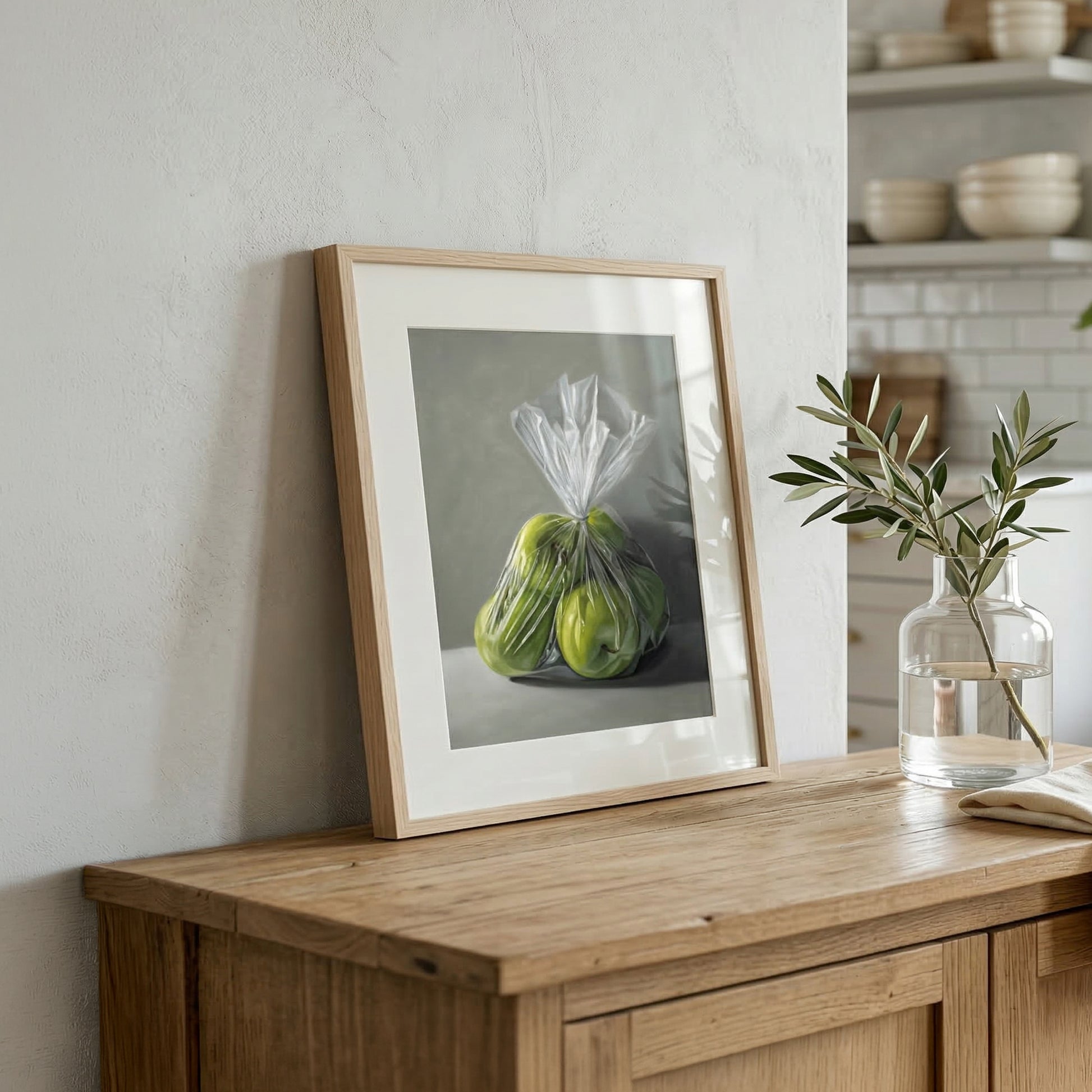 Framed Granny Smith Apples fine art print, featuring two green apples in a plastic bag, on a wooden dresser.