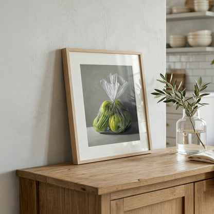 Framed Granny Smith Apples fine art print, featuring two green apples in a plastic bag, on a wooden dresser.