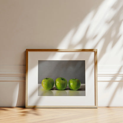 Fine art print of three vibrant green apples in a light wood frame with a white mat.