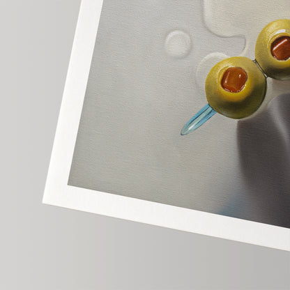 Close-up of a fine art print featuring two green olives on a blue sword pick in a light gray drink.