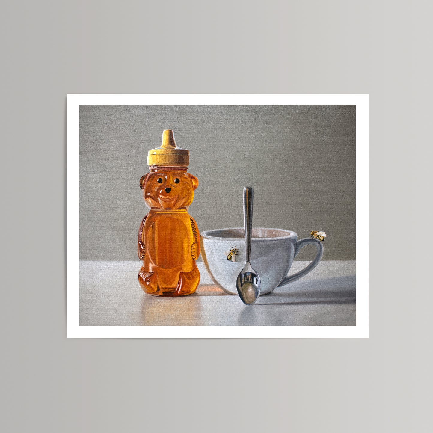 Fine art print of a honey bear bottle, white teacup with spoon, and two bees on a light background.