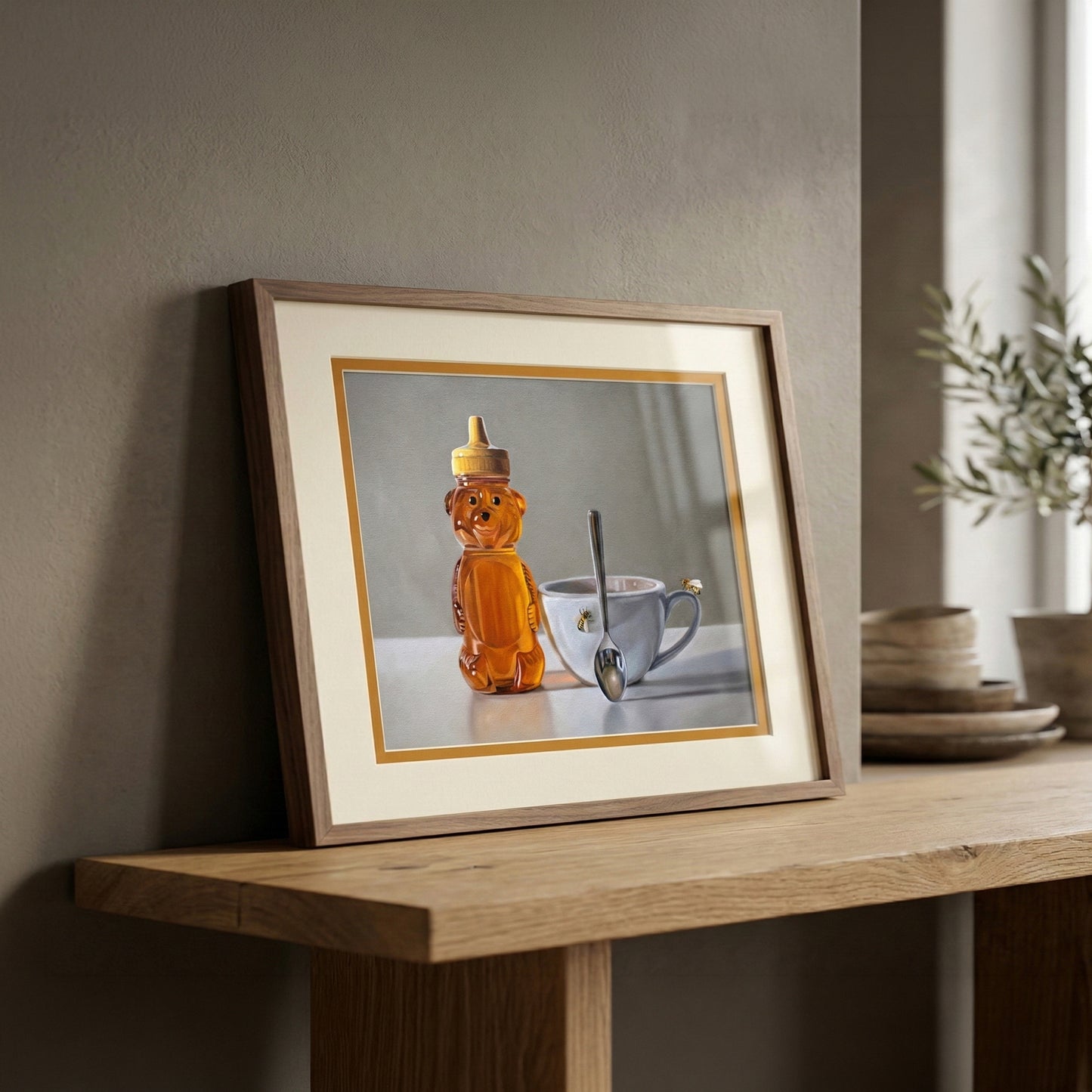 Framed fine art print of a honey bear bottle, white teacup with a bee, and spoon on a light background.