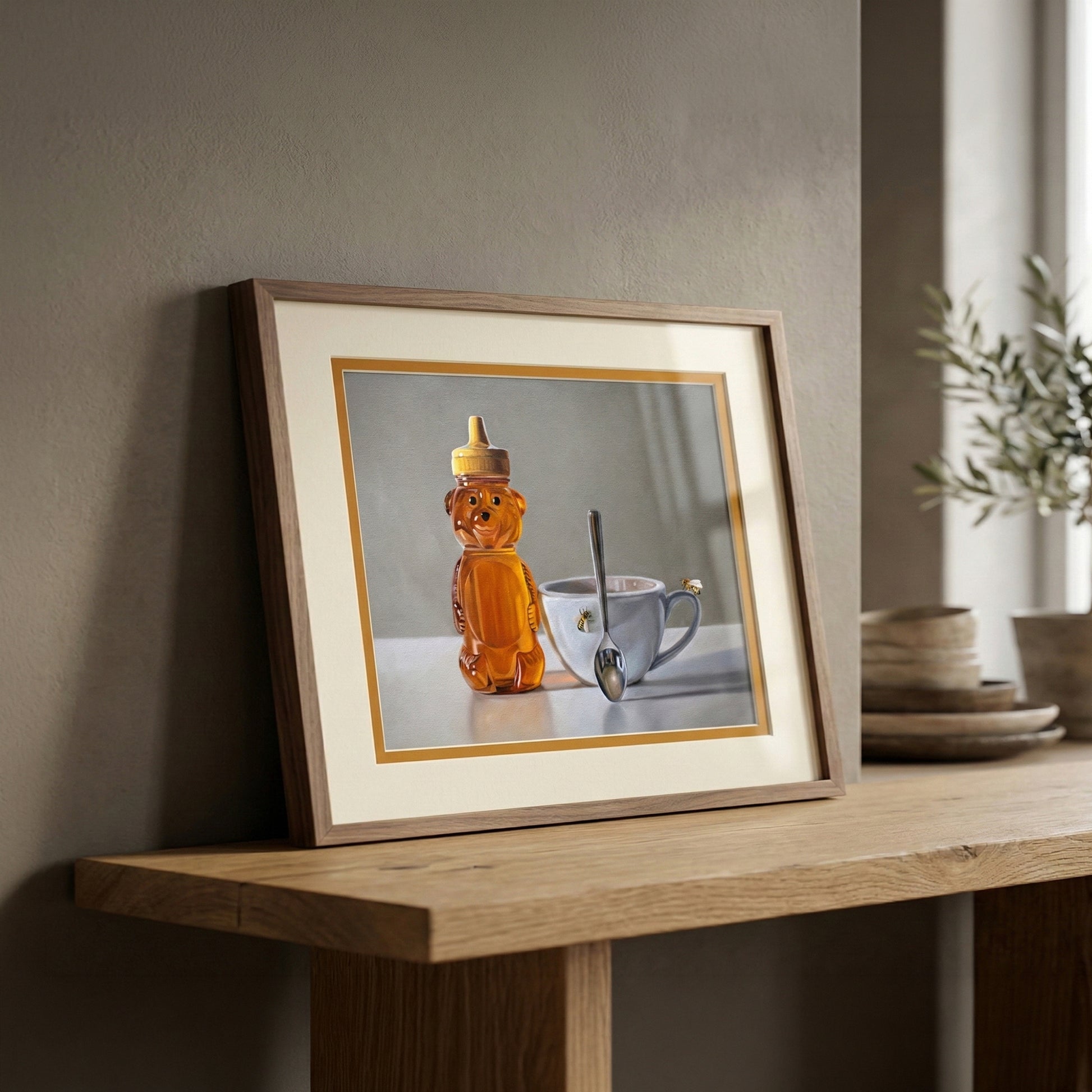 Framed fine art print of a honey bear bottle, white teacup with a bee, and spoon on a light background.