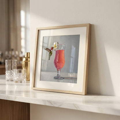 Framed fine art print of a hummingbird with a pink cocktail and plumeria flower.