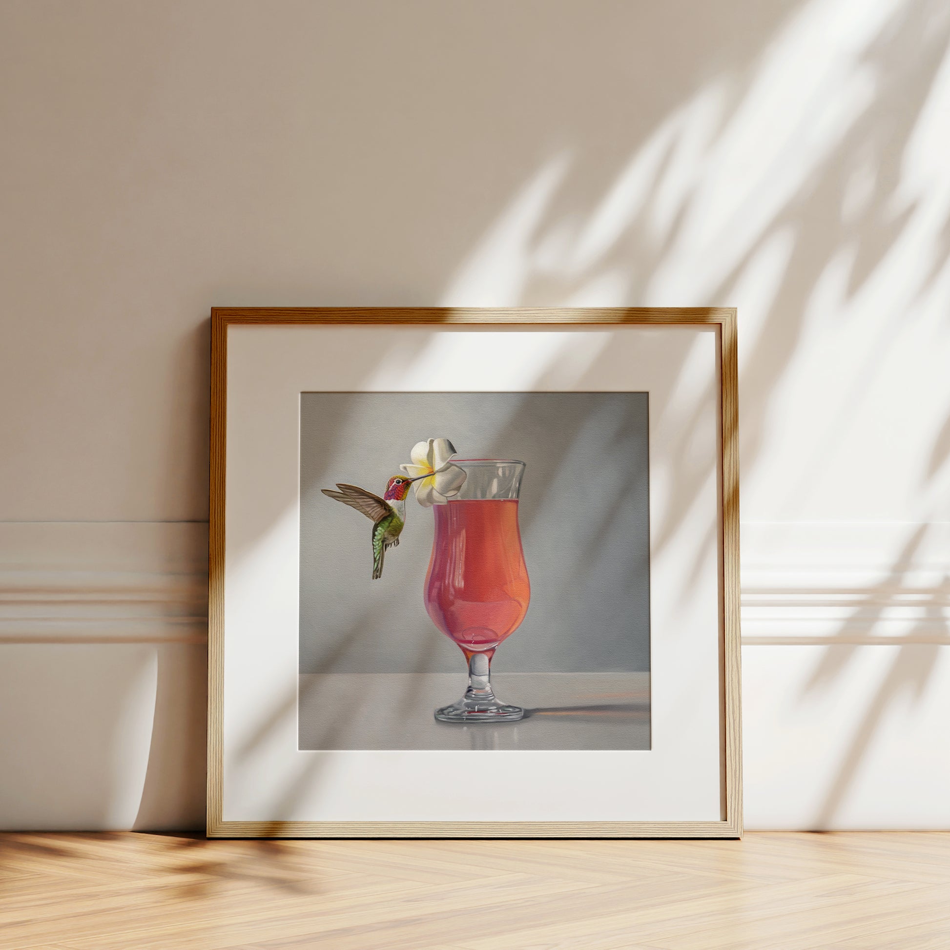 Framed fine art print of a hummingbird sipping from a pink cocktail garnished with a white plumeria flower.