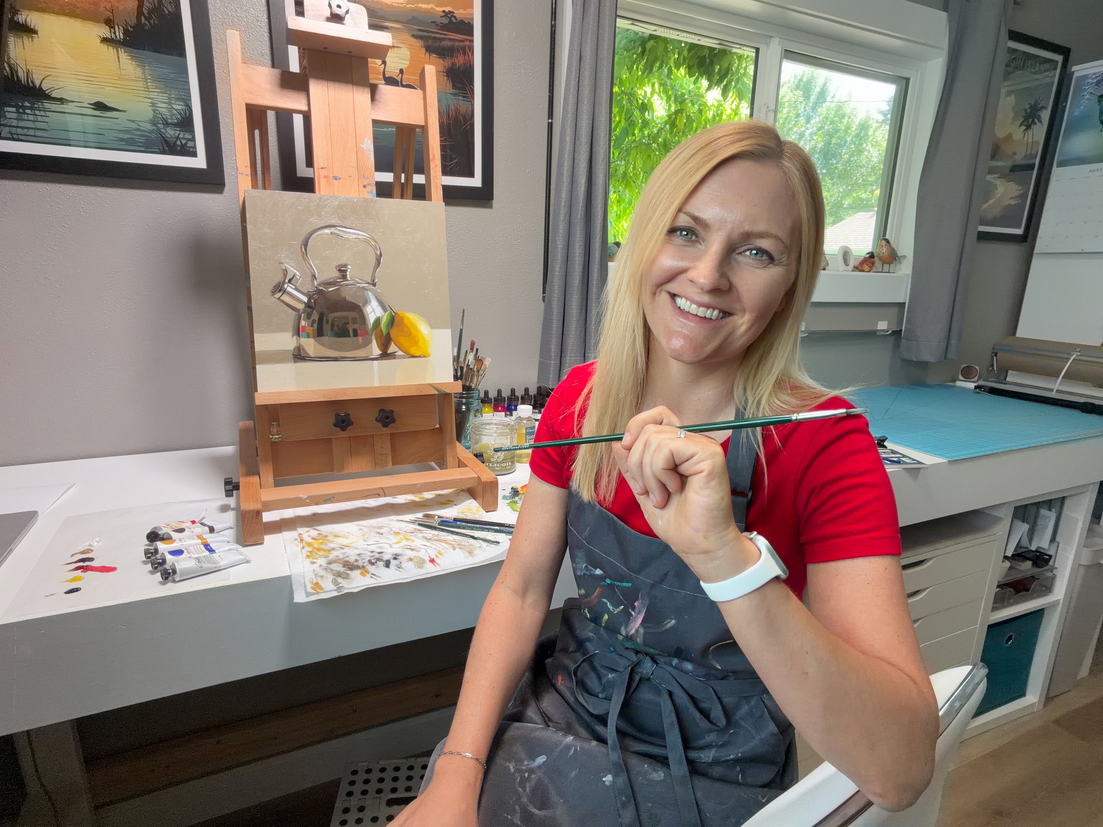 Lauren Pretorius in her studio holding a paintbrush, with art supplies and a window in the background.
