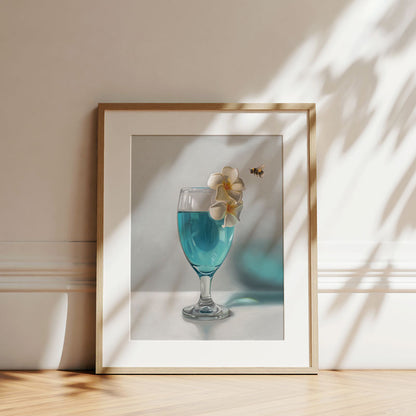 Fine art print of a blue cocktail glass with white plumeria flowers and a bumblebee, framed in a light wood frame.