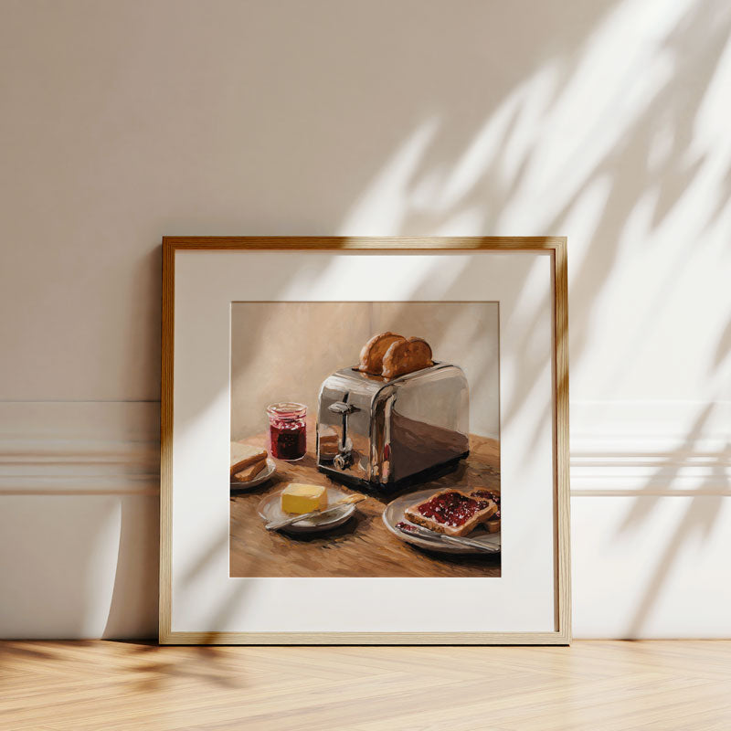 Framed fine art print of a toaster, butter, and jam on toast, displayed in a wooden frame against a white wall.
