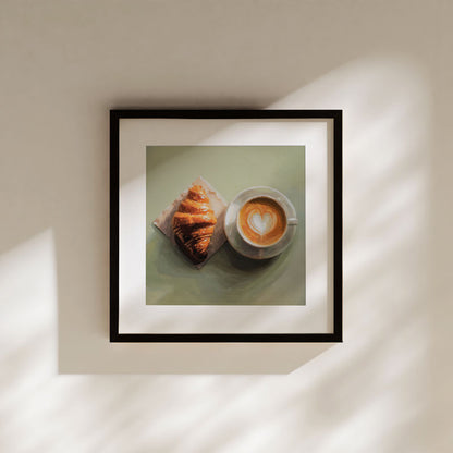 Fine art print of a croissant and latte with heart latte art, displayed in a black frame on a neutral wall.