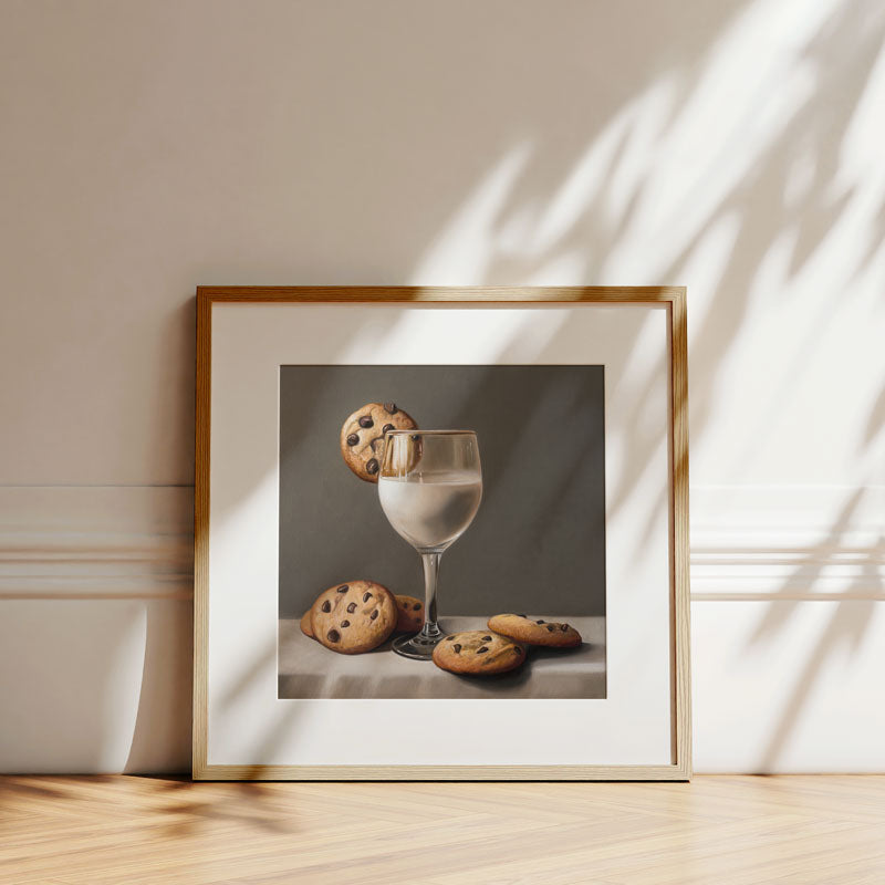 Fine art print of a glass of milk and chocolate chip cookies in a light wood frame against a neutral wall.