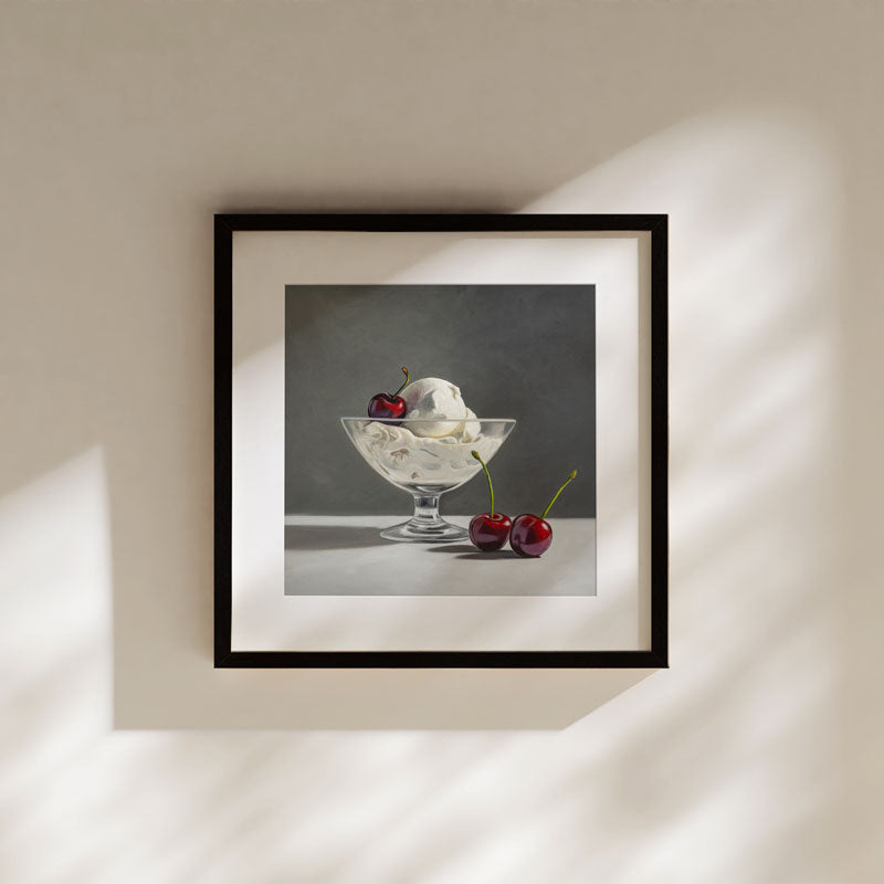 Fine art print of ice cream and cherries in a glass bowl, framed in black, displayed on a neutral wall.
