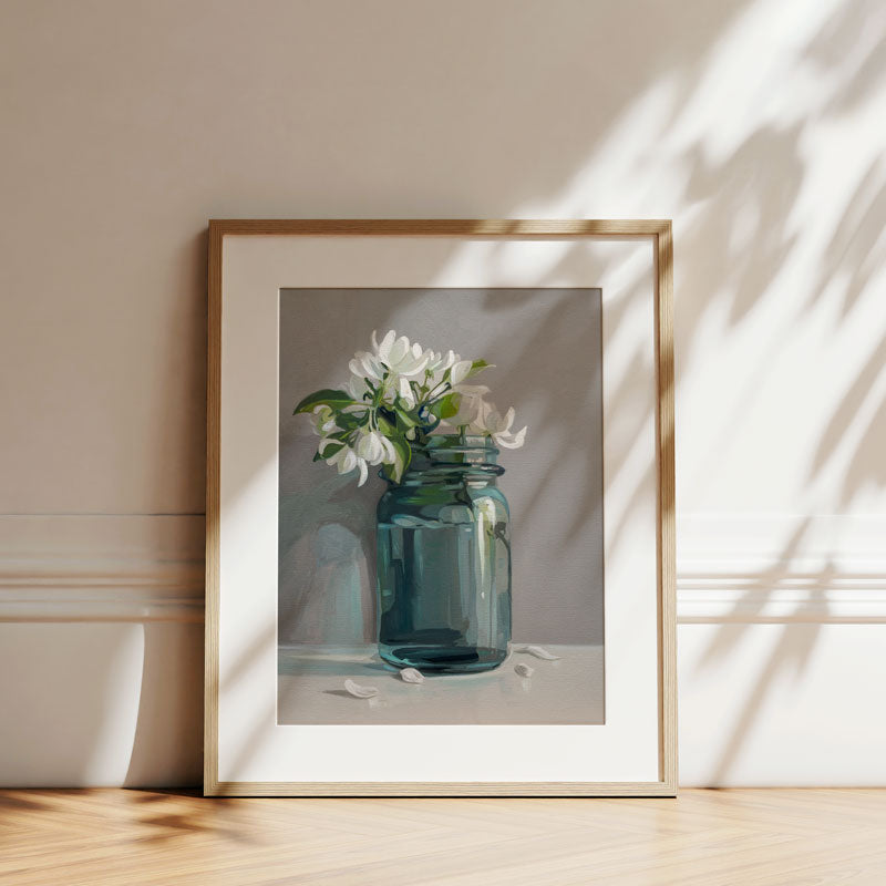 Fine art print of white apple blossoms in a teal glass jar, displayed in a light wood frame against a neutral wall.